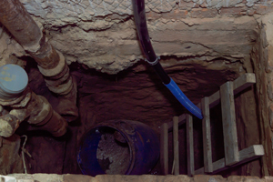 view into a deep well or pit showing pipes a blue barrel and a wooden ladder ideal for maintenance and inspection of underground areas