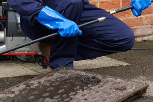 person in blue gloves using a pressure washer to clean a drain cover outdoors maintenance cleaning tools and techniques