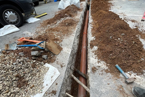 excavated trench with red pipe surrounded by dirt piles and construction tools for landscape improvement and water drainage installation