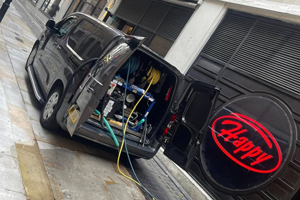 black van parked on street with open rear doors showing equipment and a large round sign that says Happy